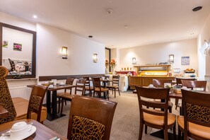 A hotel dining area with multiple tables and chairs, a buffet counter, and wall-mounted light fixtures. - Trip Inn Hotel Hamm Koblenz (Koblenz)