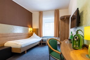 Ein Hotelzimmer mit einem Bett, einem Sessel, einem kleinen Tisch, einer Kaffeemaschine und einem an der Wand befestigten Fernseher.