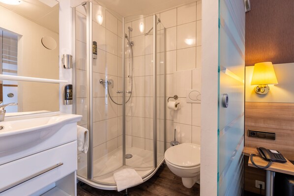 A modern bathroom with a glass-enclosed shower, a toilet, and a sink with a mirror.