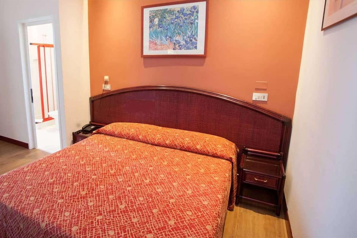 A bedroom with a wooden bed, a nightstand, a door, and a painting on the wall.