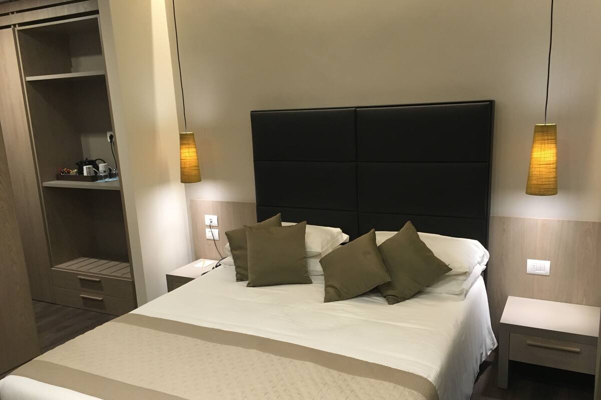 A hotel room with a large bed, two bedside tables, a wardrobe, and a nightstand with a lamp.