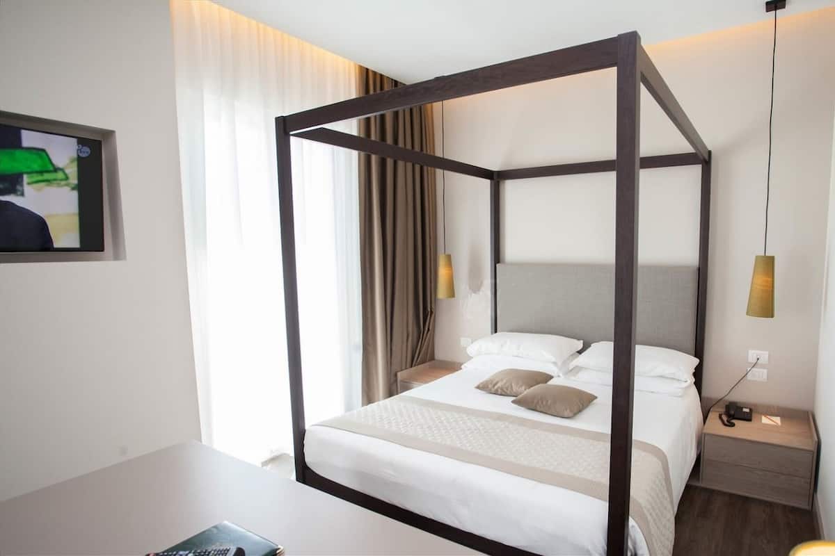 A four-poster bed with a headboard, two bedside tables, a bedside lamp, and a framed picture on the wall.