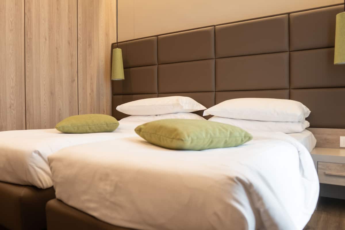 A neatly made bed with white and green pillows, a wooden headboard, and a wooden floor.