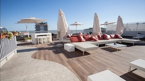 A rooftop lounge with white sofas, red cushions, and white umbrellas. - Principe Palace (Jesolo)