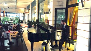 A grand piano in a well-lit indoor space with tables and chairs, suggesting a lounge or waiting area. - Principe Palace (Jesolo)