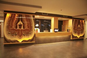A reception desk with a large, patterned wall design, a flat-screen TV, and a potted plant. - Delfina Palace (Foligno)