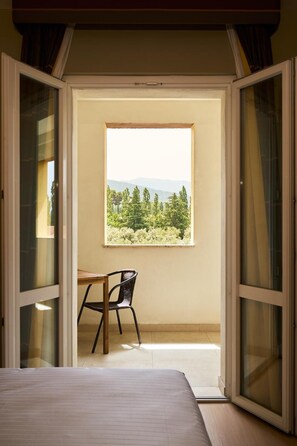 A bedroom with a bed, a chair, and a window with a view of trees and mountains. - Delfina Palace (Foligno)