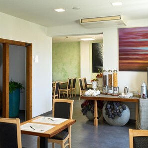 A dining area with wooden tables and chairs, a coffee station, and a large abstract painting on the wall. - Delfina Palace (Foligno)