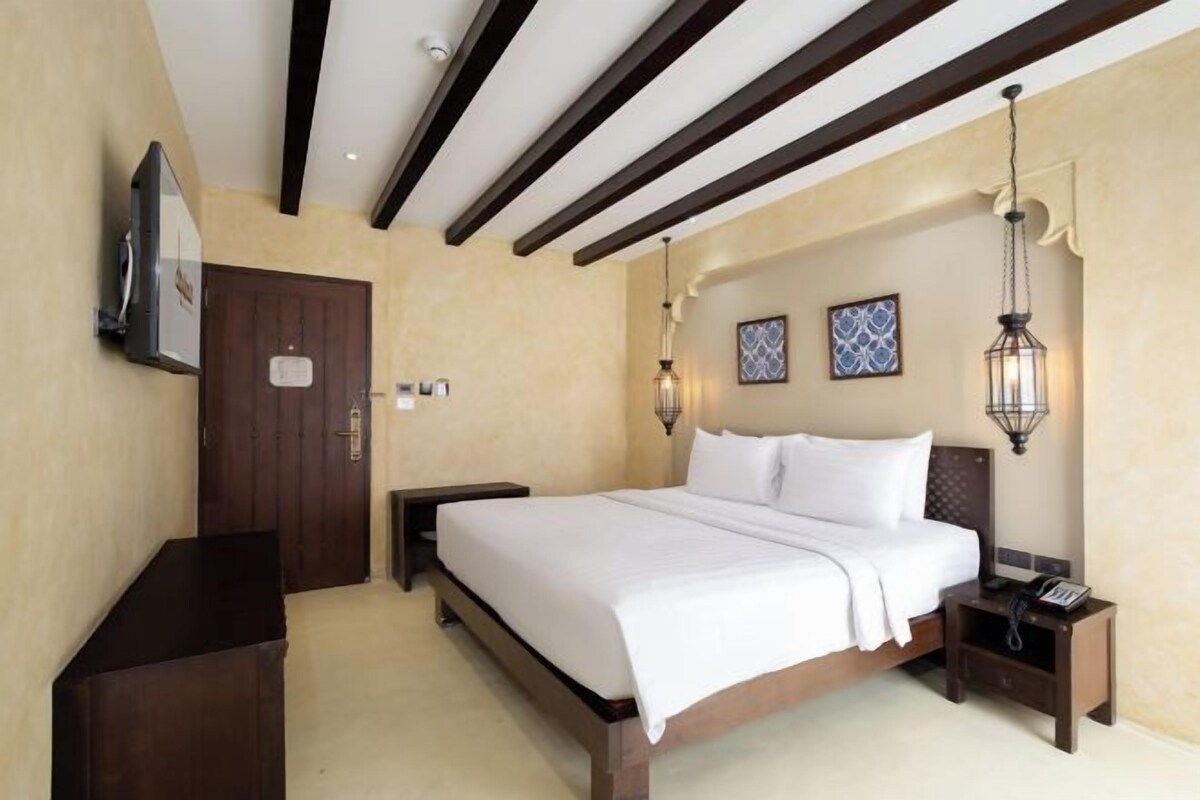 A hotel room with a large bed, wooden headboard, two bedside tables with lamps, a flat-screen TV, and a door.