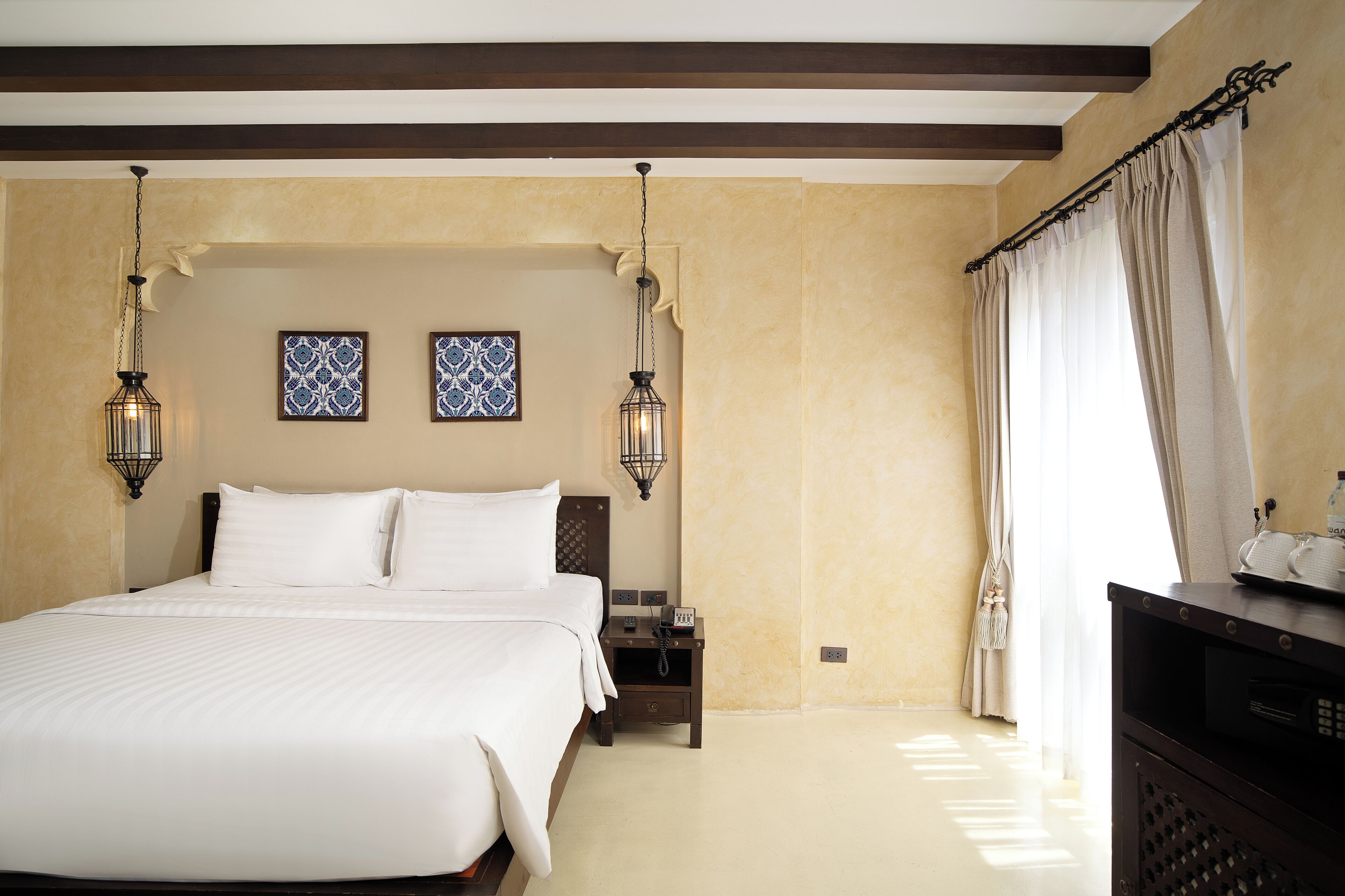 A hotel room with a large bed, two wall-mounted lamps, a nightstand, and a window with curtains.
