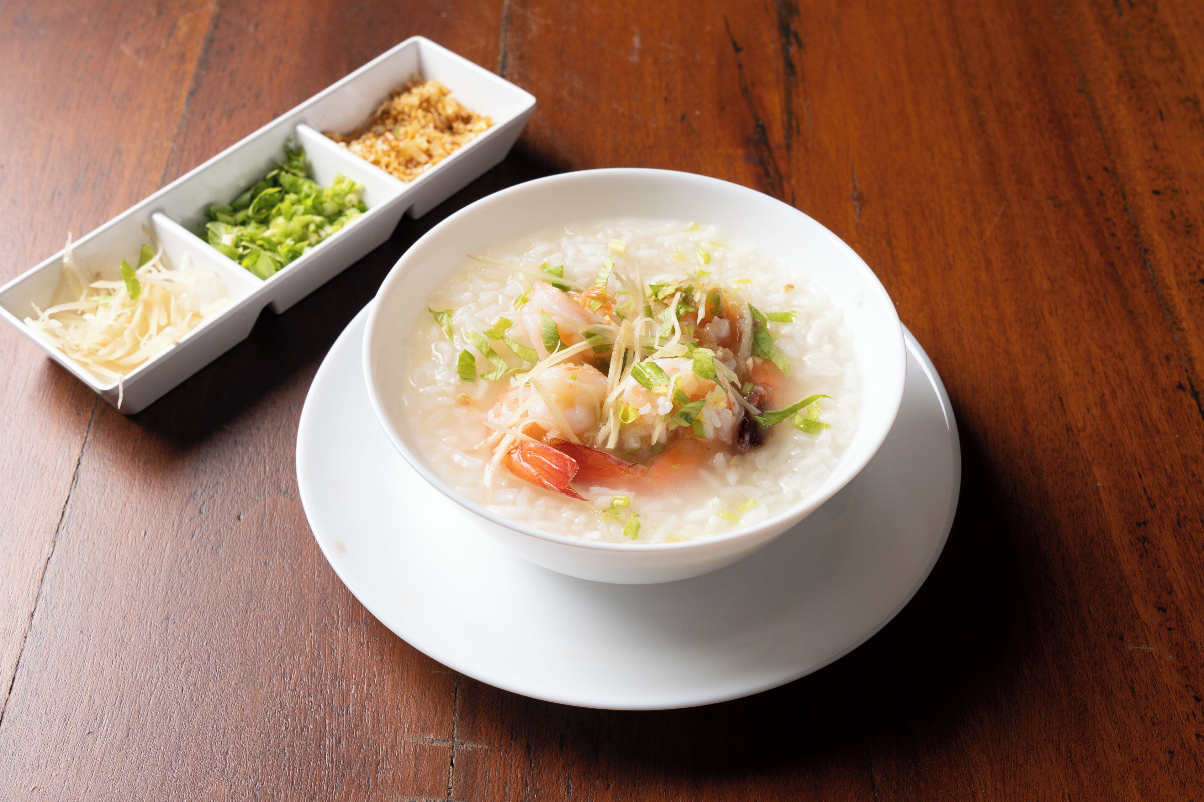 A bowl of soup with shrimp and vegetables on a wooden table.