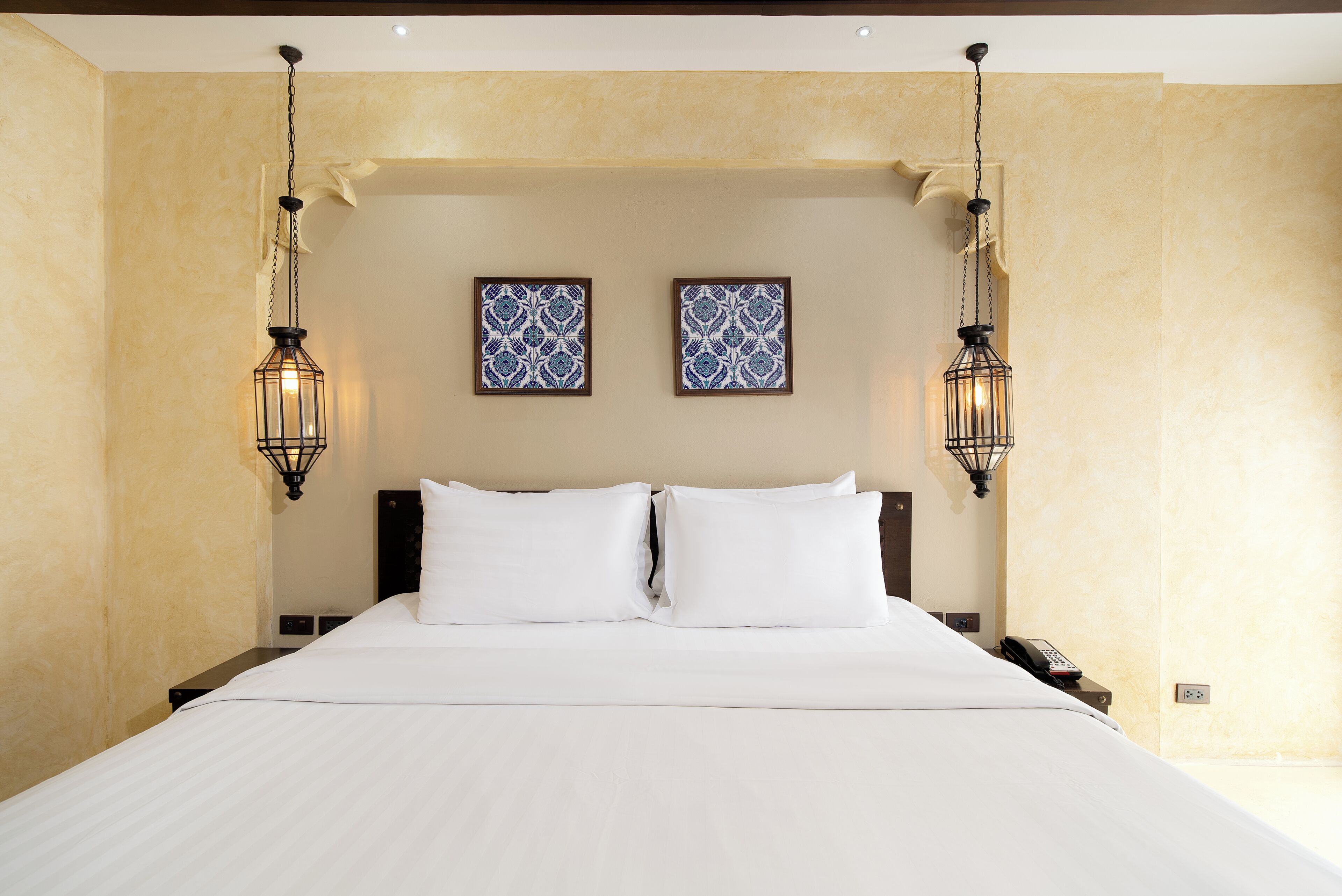 A hotel room with a large bed, two wall-mounted light fixtures, and two framed wall art pieces.