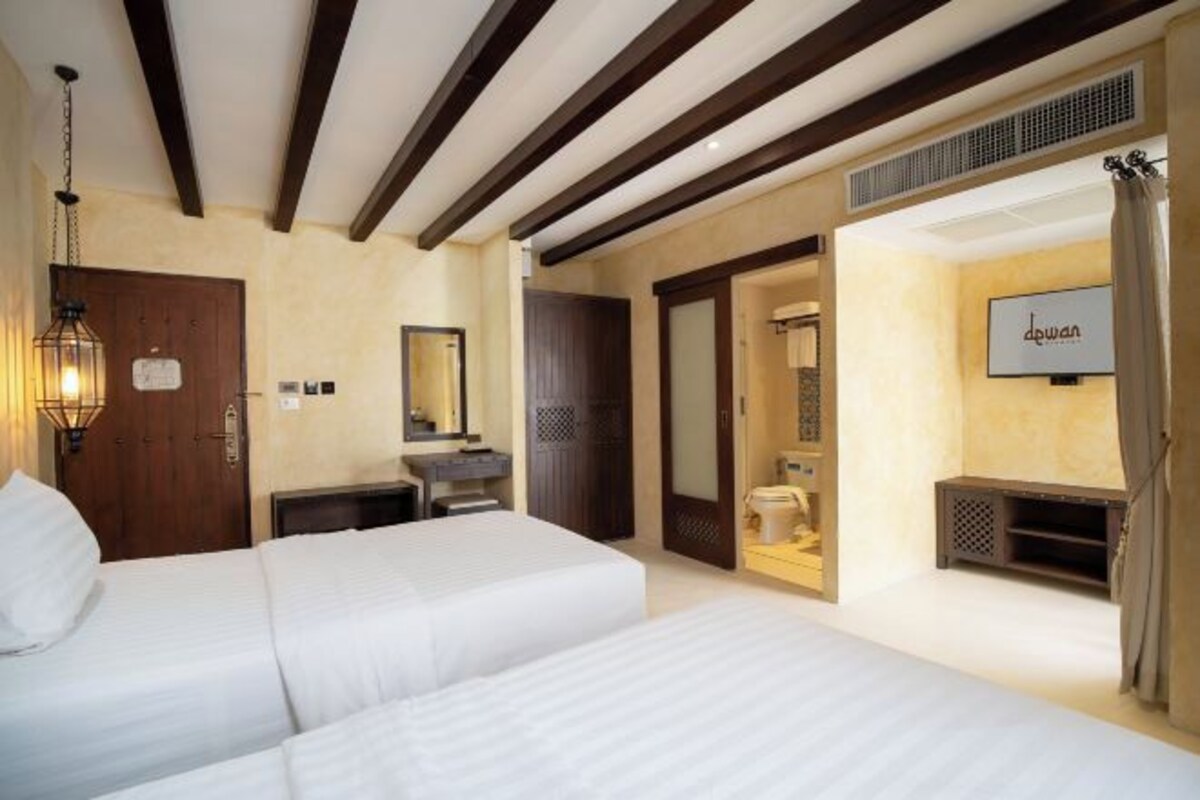 Une chambre d’hôtel avec deux lits, un plafond en bois, une salle de bain avec un miroir et un téléviseur fixé au mur.