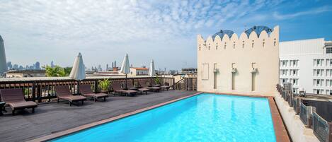A rooftop pool with lounge chairs and a castle-like building in the background.