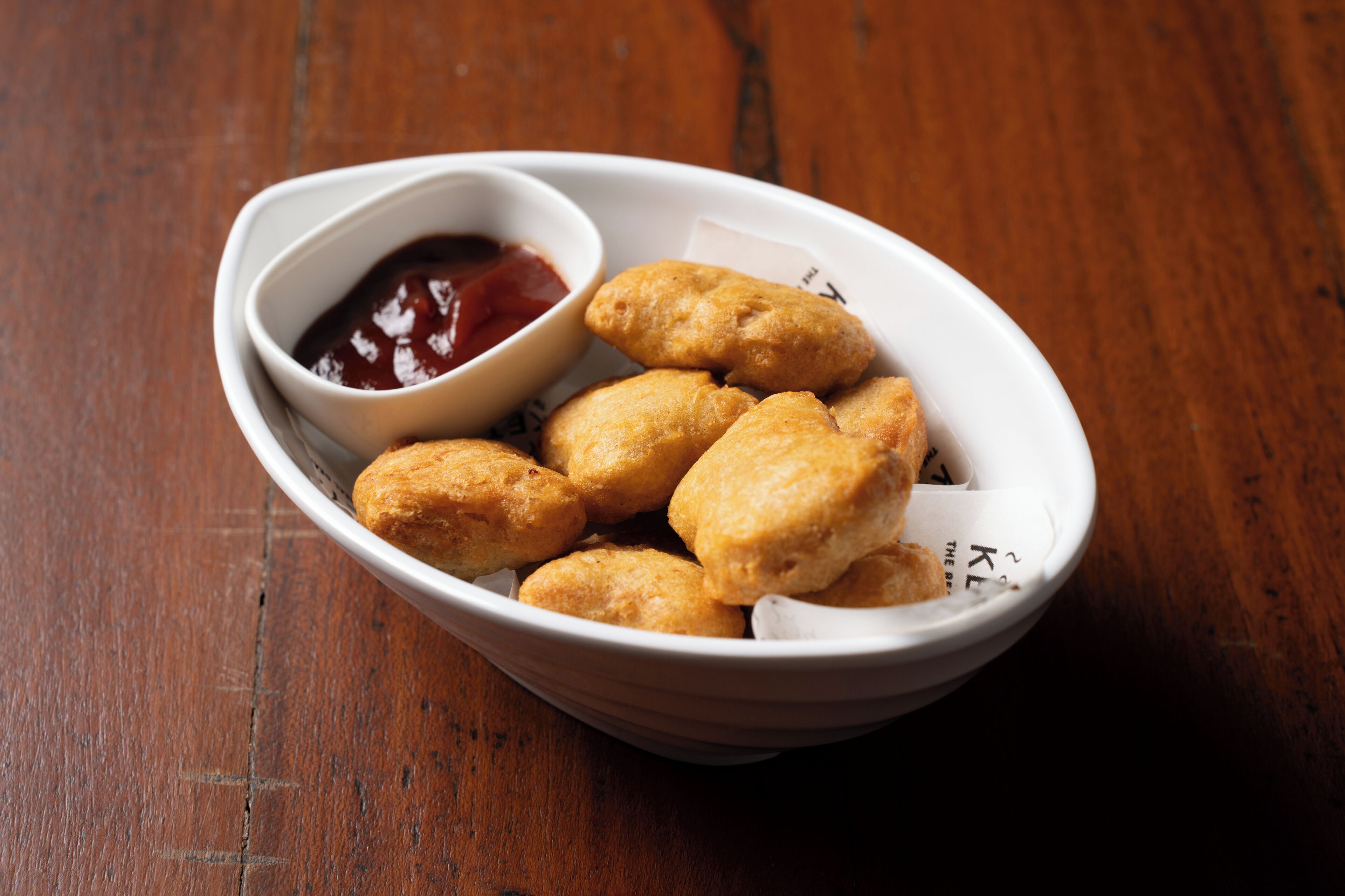 A white bowl containing several golden-brown fried items and a small bowl of red sauce.