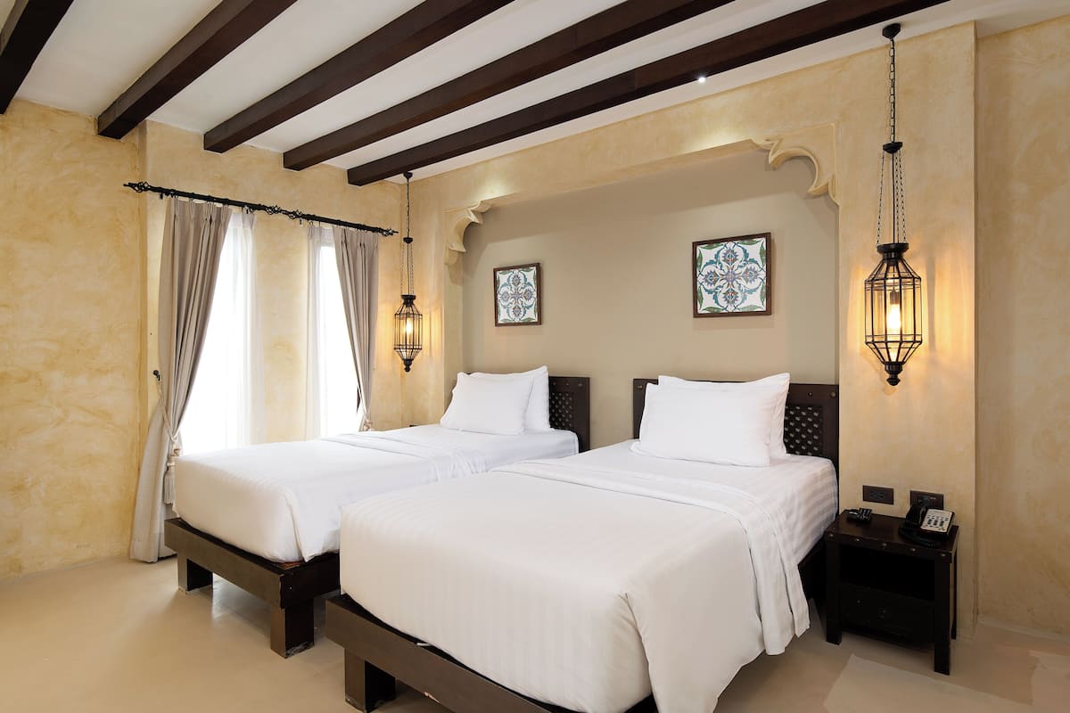A hotel room with two beds, a nightstand, and decorative wall sconces.