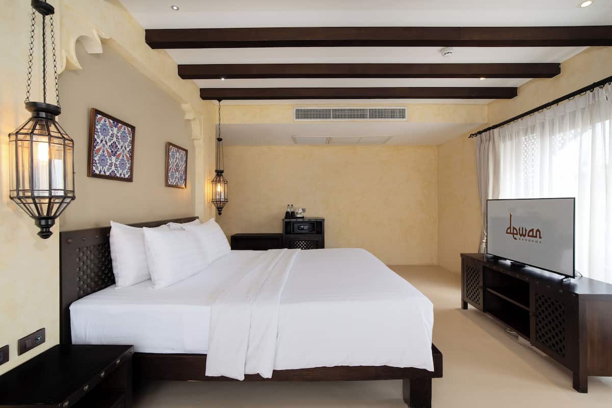 A hotel room with a large bed, a TV on a stand, and two wall-mounted lamps.