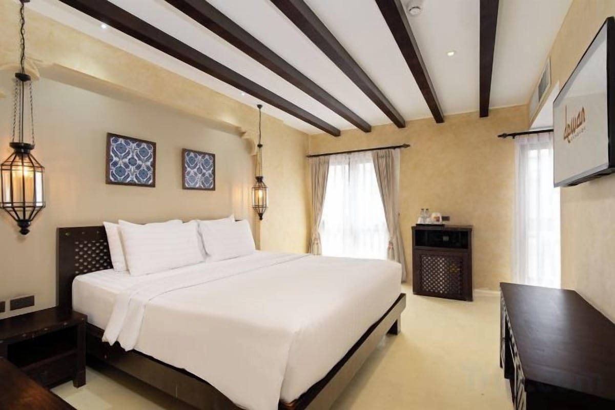 A hotel room with a large bed, bedside tables, a dresser, and wall-mounted artwork.