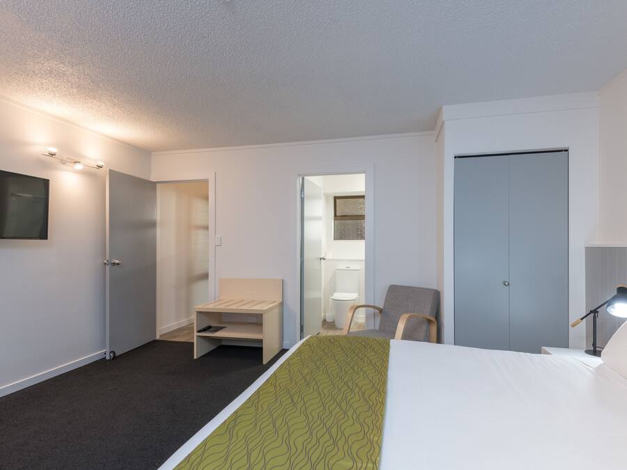A hotel room with a bed, a desk, a chair, a TV, and a wardrobe.