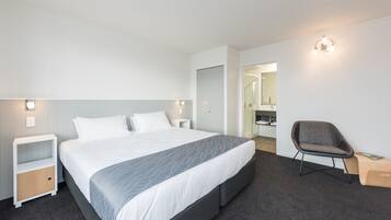 A modern hotel room with a large bed, bedside tables, a chair, and a bathroom visible through an open door.
