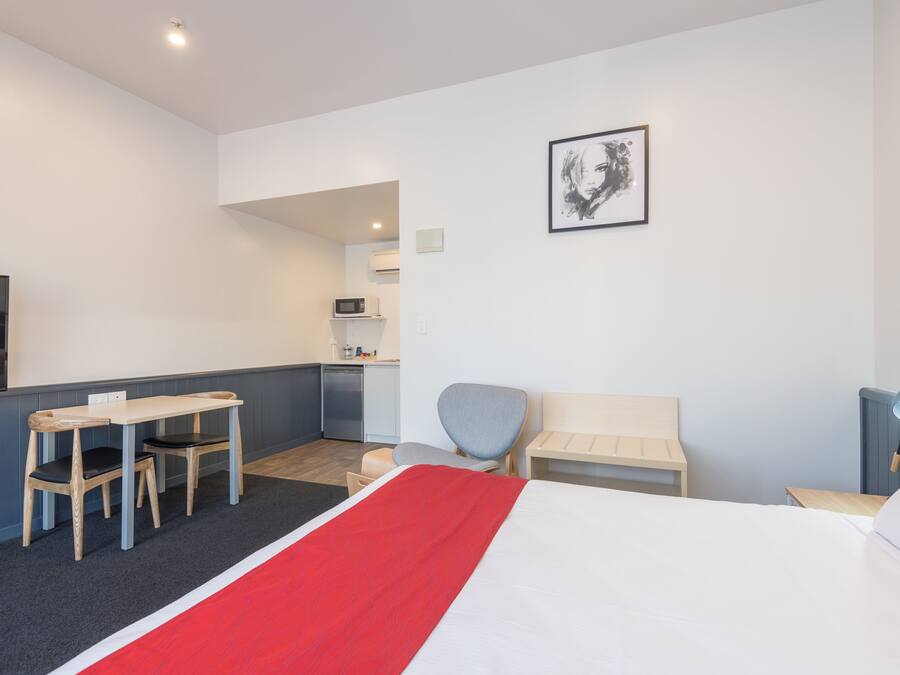 Une chambre d’hôtel comprenant un lit, un bureau avec des chaises, une petite kitchenette, un téléviseur et un tableau encadré au mur.