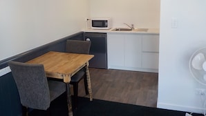 A compact kitchen with a microwave, sink, and refrigerator. There is a dining table with two chairs.