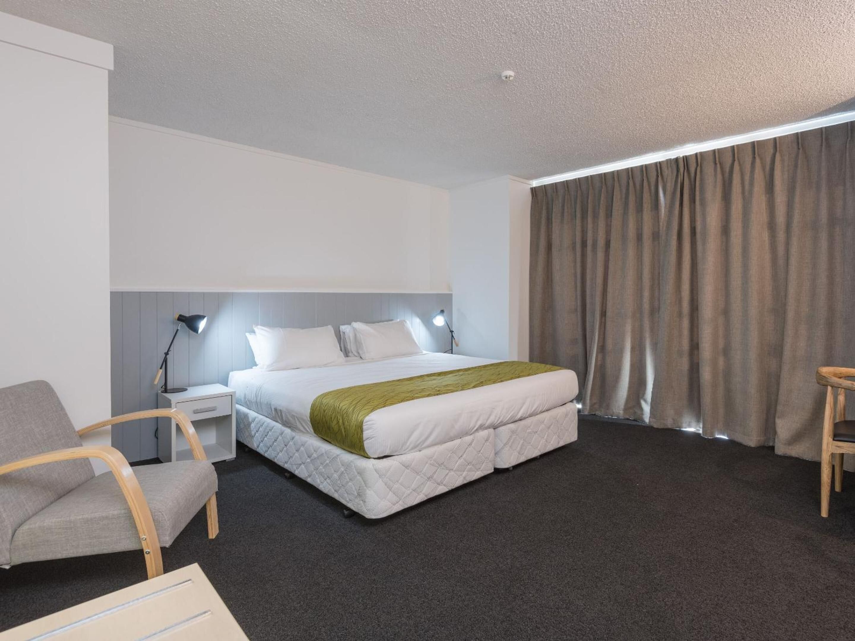 A hotel room with a bed, a desk, a chair, and a window with curtains.