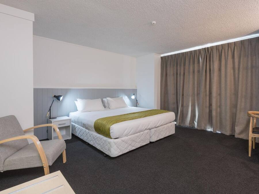 A hotel room with a bed, a desk, a chair, and a window with curtains.