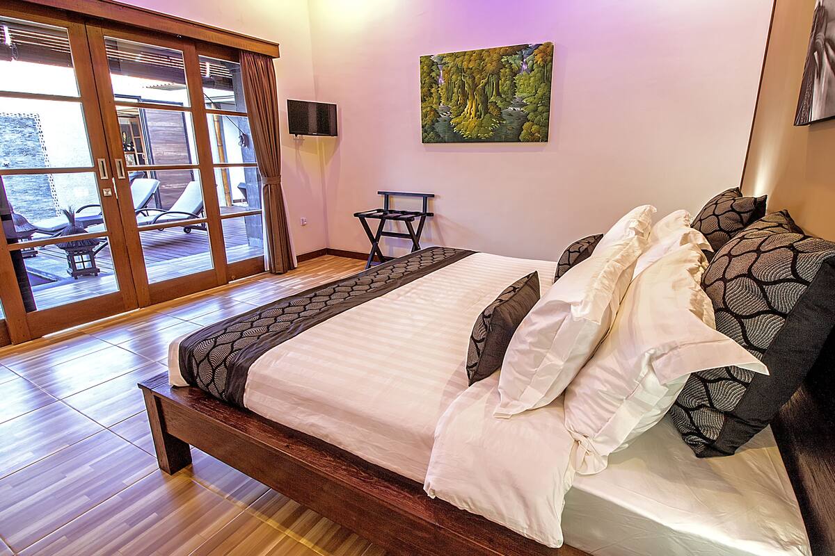 Ein Schlafzimmer mit einem großen Bett, einem Fernseher, einem Gemälde und Blick auf eine Außenbestuhlung.