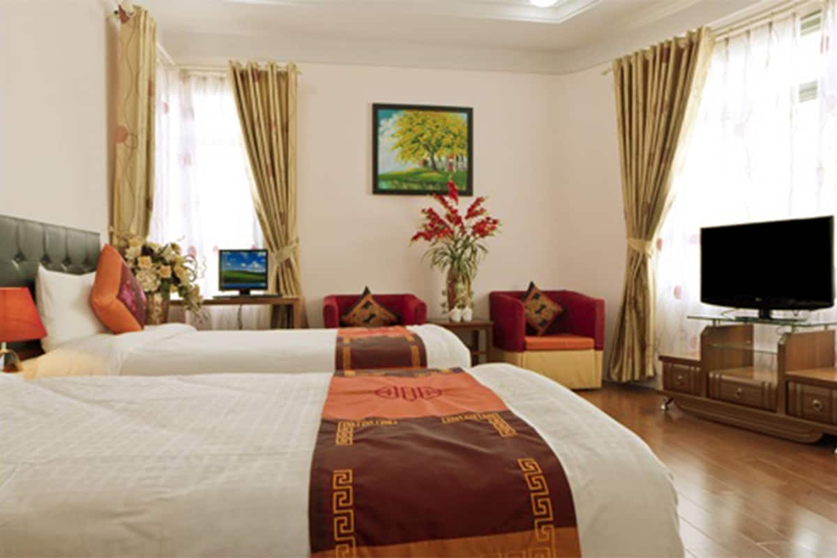 A hotel room with two beds, a television, a desk, and a vase with flowers.