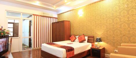 A bedroom with a wooden bed, a TV, a wardrobe, and a nightstand with a lamp.