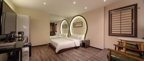 A hotel room with a bed, a desk with a computer, a small table, and a chair.