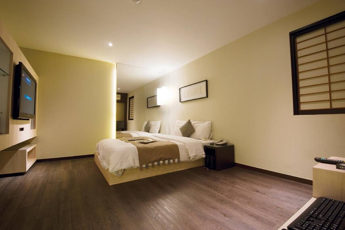 Een hotelkamer met een bed, nachtkastje, televisie en een raam met zonwering.