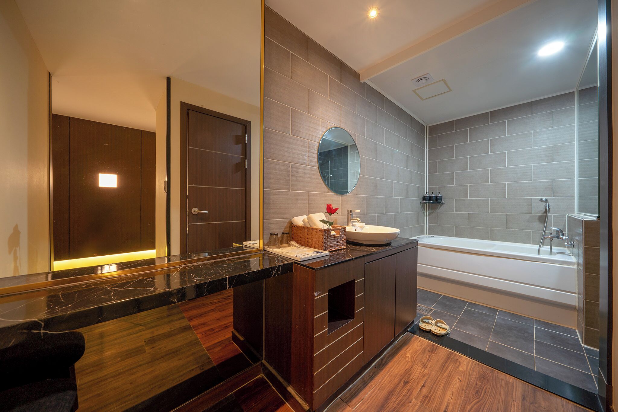 A modern bathroom with a marble countertop, a round mirror, a bathtub, and a shower area.