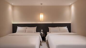 Una habitación de hotel con dos camas, un cabecero oscuro, una mesita de noche con lámpara e iluminación colgante.