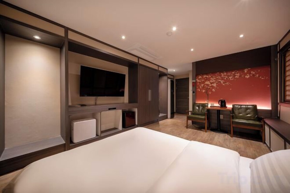 A hotel room with a large bed, a flat-screen TV mounted on the wall, a seating area with a table and chairs, and a decorative wall.