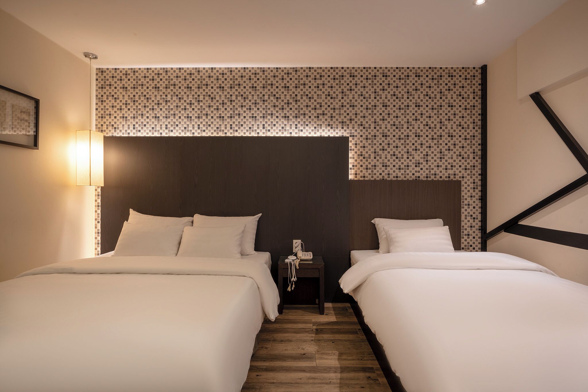 A hotel room with two beds, a nightstand with a telephone, and a wall with a mosaic tile design.