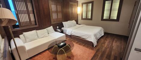 A bedroom with a bed, a sofa, a coffee table, and wooden flooring.