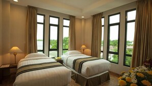 Habitación de hotel con dos camas, ventanas amplias y vistas al verdor.