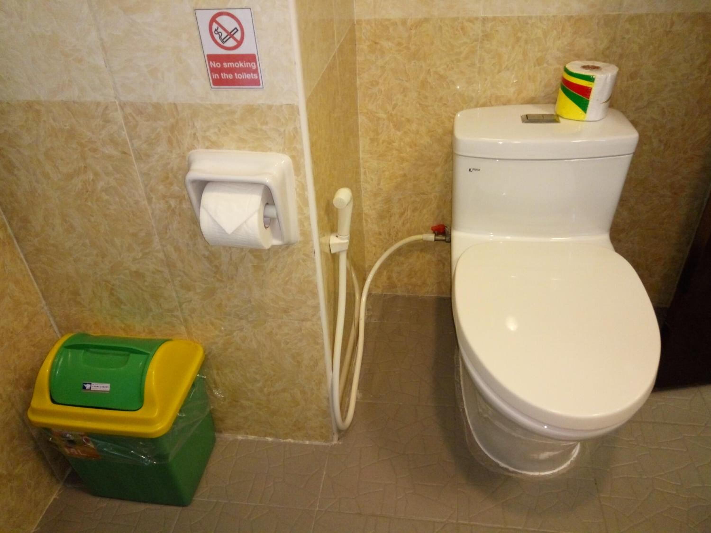 Un baño con inodoro, dispensador de toallas de papel, rollo de papel higiénico y cubo de basura.