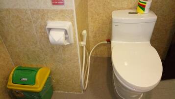 Un baño con inodoro, dispensador de toallas de papel, rollo de papel higiénico y cubo de basura.