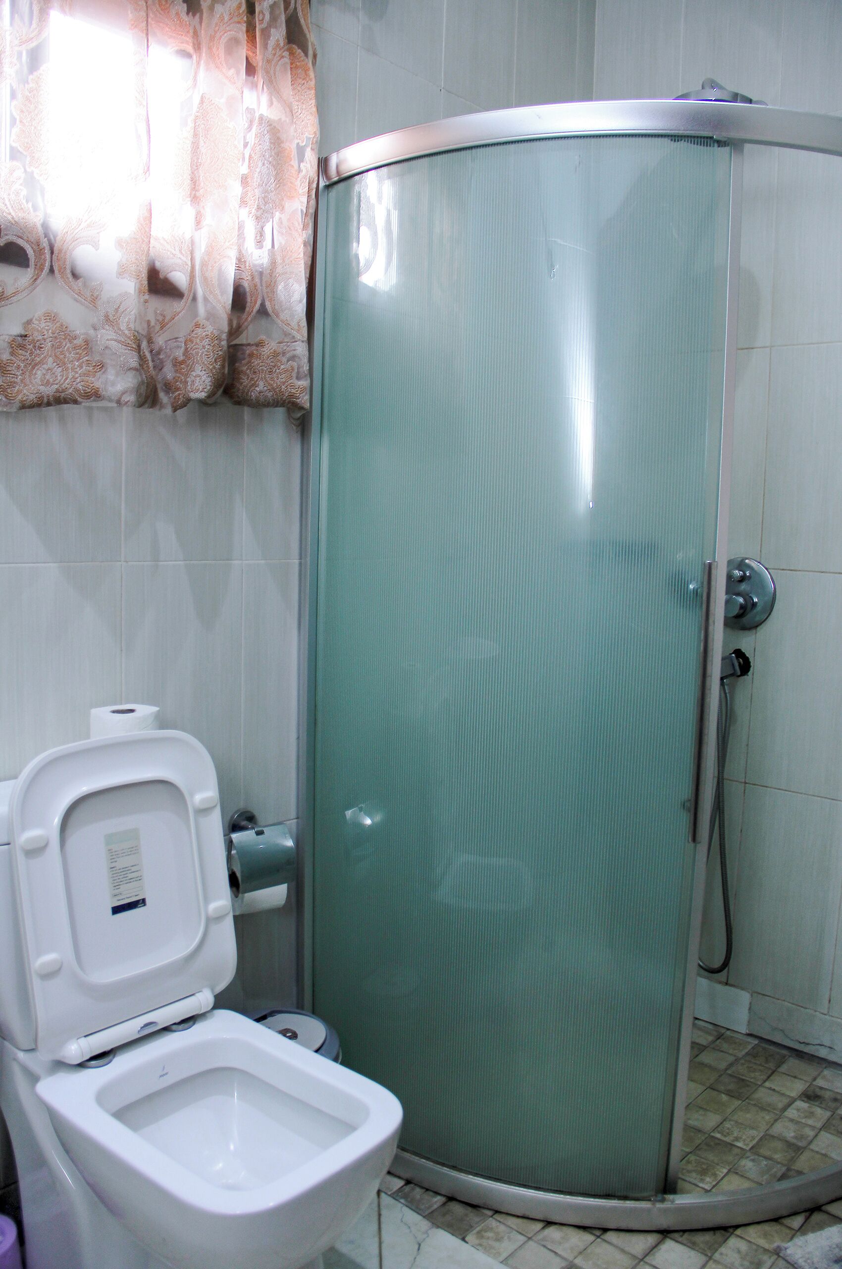 Een badkamer met toilet, douchecabine en toiletpapierhouder.