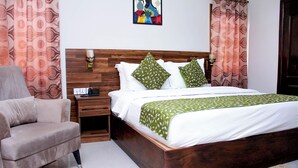Een slaapkamer met een houten hoofdbord, een bed met witte beddengoed en groene kussens met een patroon, een nachtkastje met een lamp en een stoel.