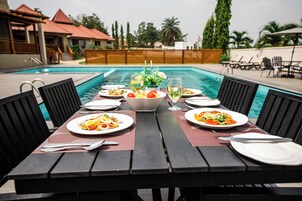 A dining table with plates of food and drinks, set against a poolside view.