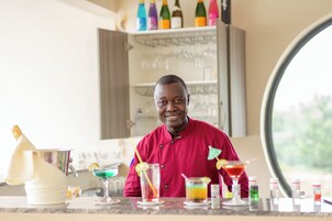 A person in a red shirt standing behind a bar with various drinks and bottles.