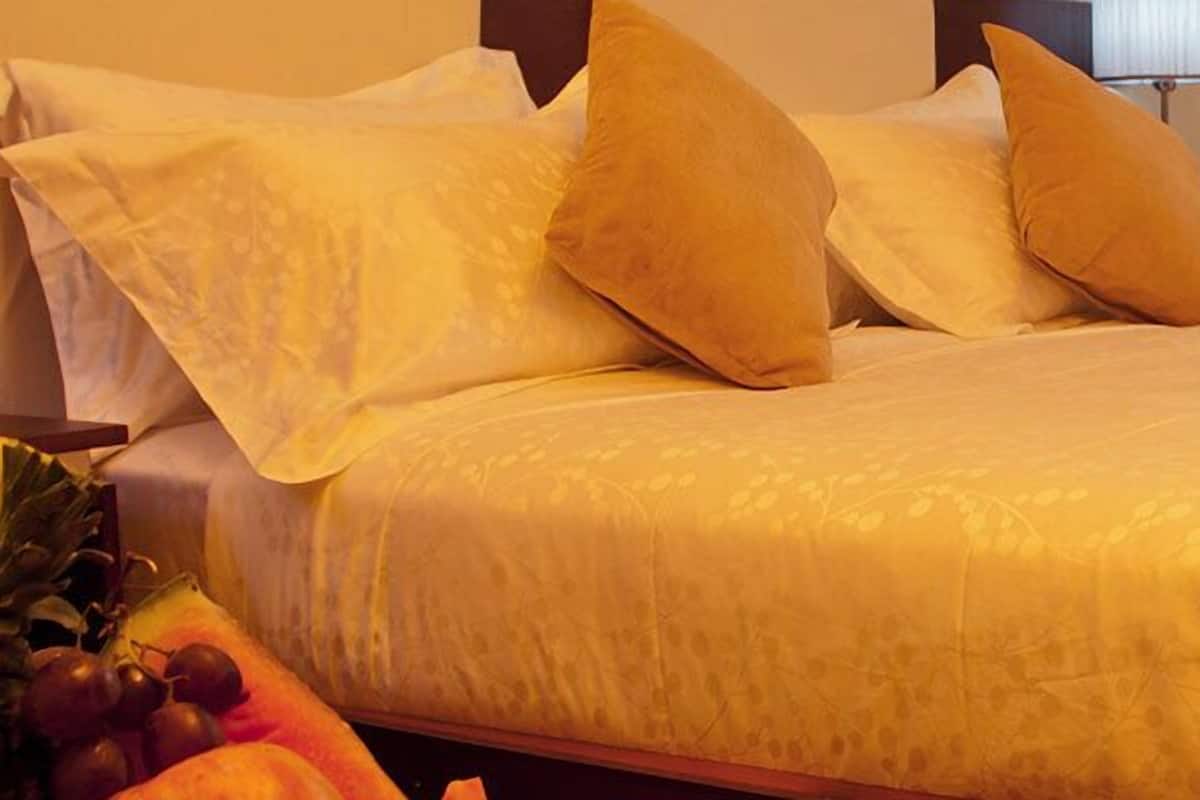A hotel room with a bed, pillows, a nightstand, a lamp, and a fruit basket.