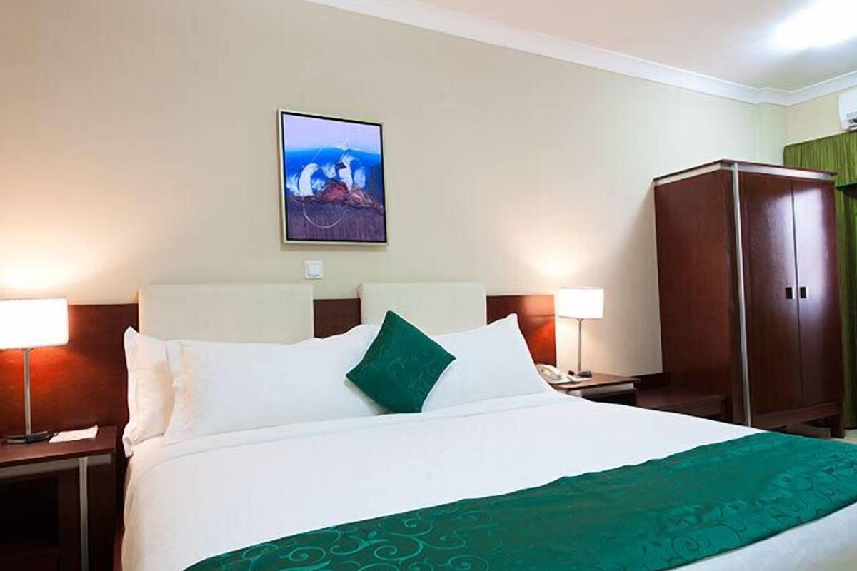 A hotel room with a bed, two bedside lamps, a nightstand, a wardrobe, and a painting on the wall.