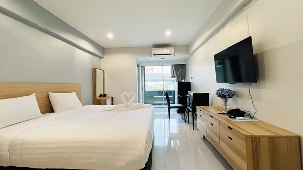 A hotel room with a large bed, a wooden dresser, a desk with a chair, a flat-screen TV mounted on the wall, and a window with a view of the city. - 14 Avenue (Bangkok)