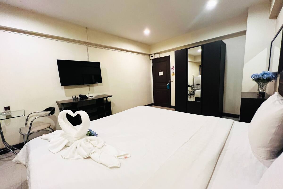 A hotel room with a bed, a TV mounted on the wall, a desk with a chair, and a mirror.