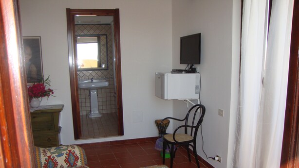 Une petite pièce agréable et chaleureuse, avec un canapé, un fauteuil, une petite table sur laquelle est posé un vase de fleurs, un miroir, un téléviseur et une fenêtre avec des rideaux.